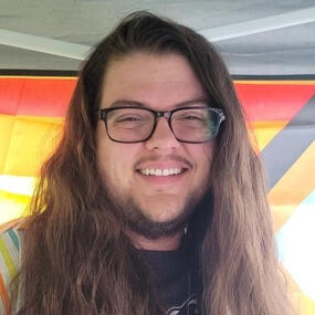 Headshot of a white man with long brown hair, black glasses, and a short brown beard.